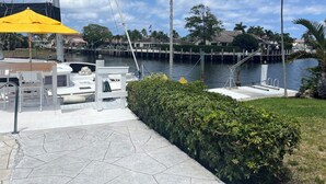 A marina with boats docked, a yellow umbrella, and a view of the water and houses in the background. - Bright Spacious 3bed/2bath Intracoastal Home (Deerfield Beach)