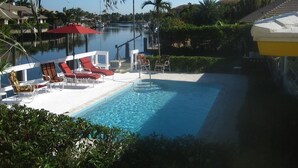 A pool area with lounge chairs and a small boat docked by the water. - Bright Spacious 3bed/2bath Intracoastal Home (Deerfield Beach)