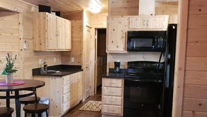 A compact kitchen with wooden cabinets, a microwave, and a black oven. There is a small dining area with stools and a table. - Christopher Creek Cabins - Cabin 3 (Payson)