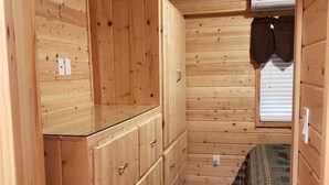 A wooden cabin room with a bed, a window with curtains, and a built-in wardrobe. - Christopher Creek Cabins - Cabin 3 (Payson)
