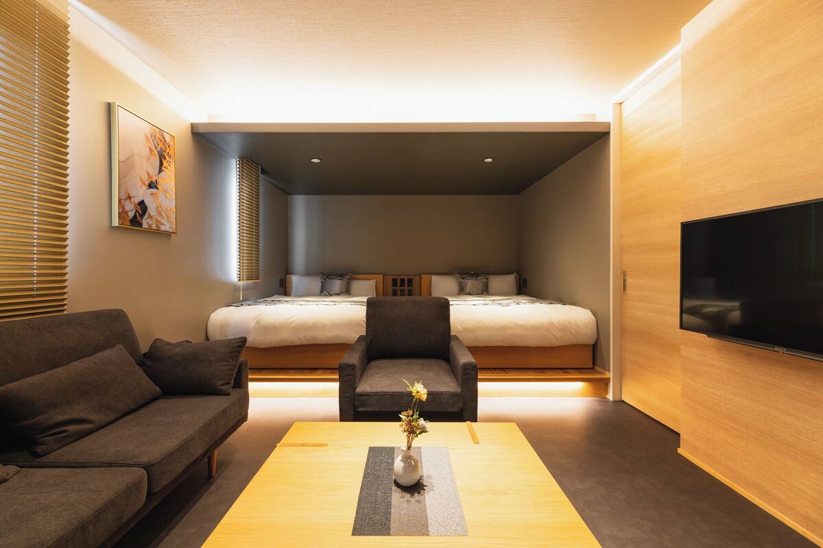 Ein modernes Hotelzimmer mit Bett, Sofa, Fernseher und einer Vase mit Blumen auf dem Couchtisch.