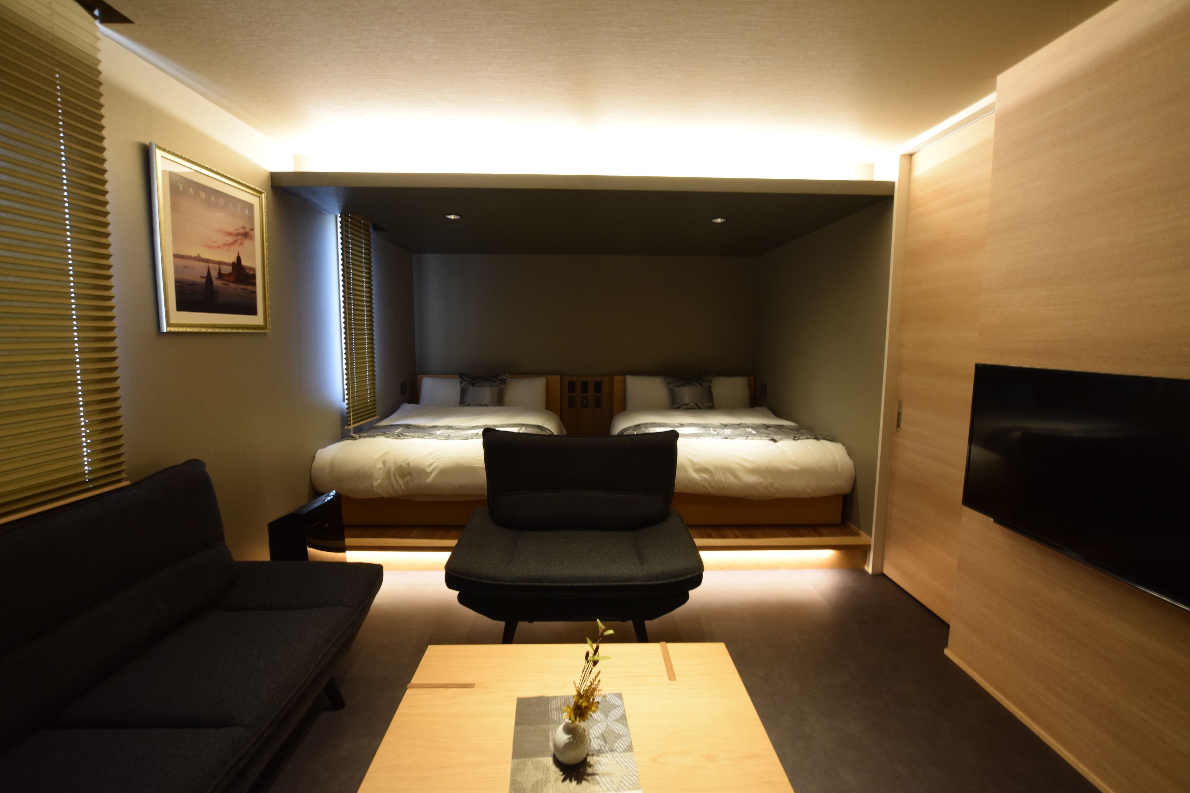 A modern hotel room with a bed, a sofa, a TV, and a small table with a vase.