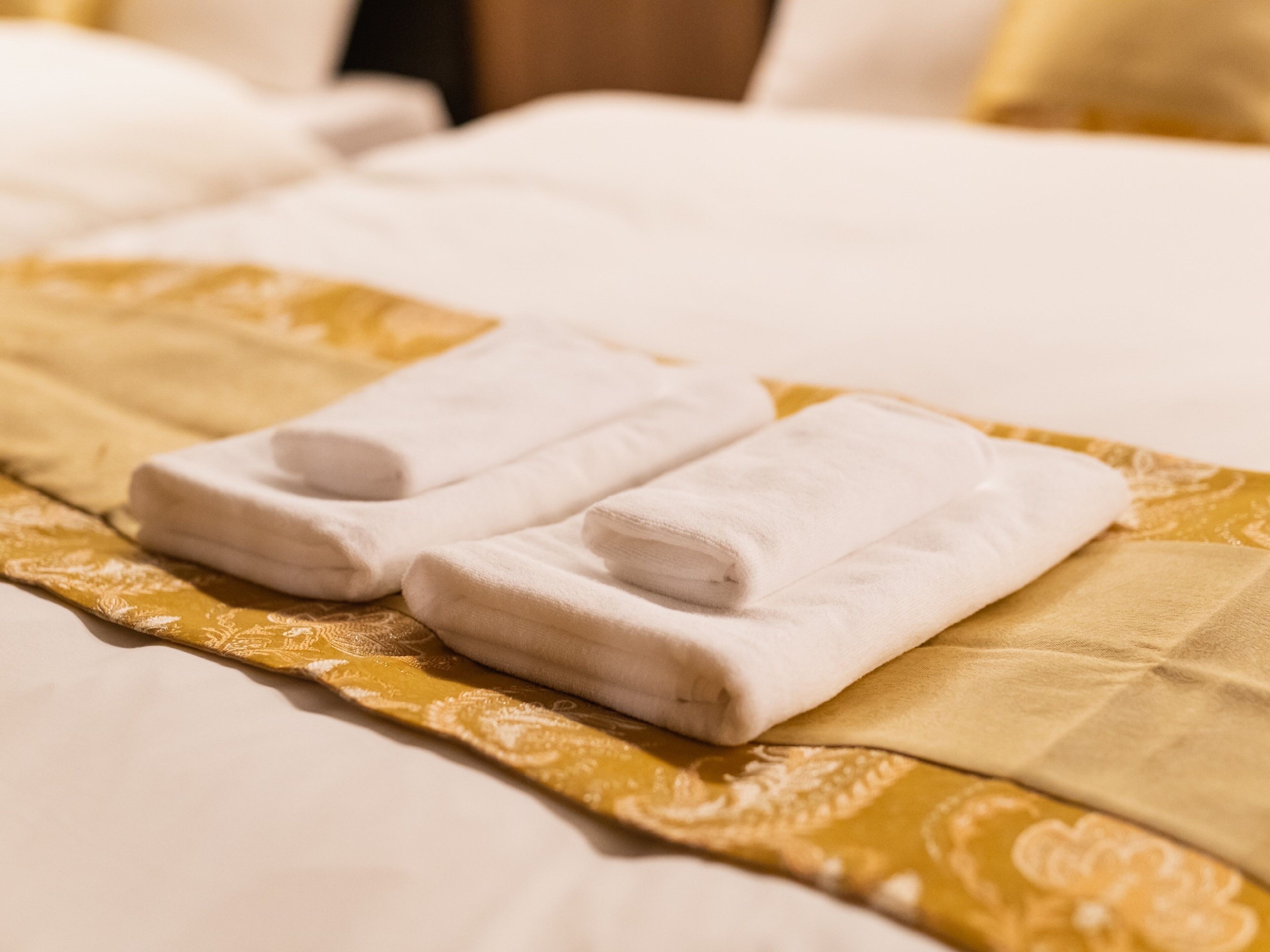 A neatly made bed with a gold-patterned bedspread and two folded white towels placed on it.