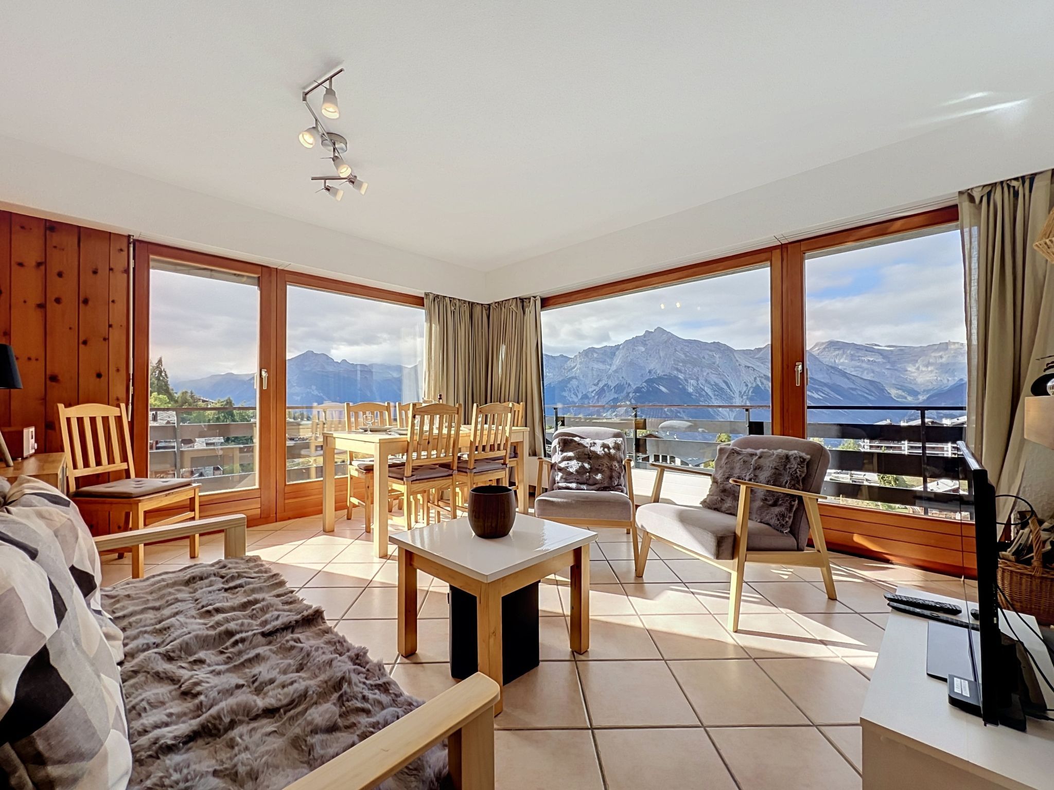 Un salon spacieux doté d’une grande fenêtre offrant une vue sur les montagnes, de meubles en bois et d’un luminaire moderne au plafond.