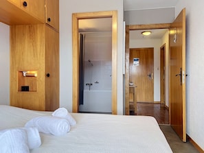 Ein Hotelzimmer mit Bett, einem Holzschrank, einem Badezimmer mit Dusche und einer Tür zu einem weiteren Raum.