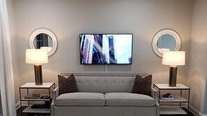Una sala de estar moderna con un sofá gris, dos sillones, una mesa de centro y un televisor de pantalla plana montado en la pared.