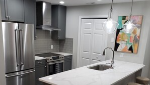 Una cocina moderna con electrodomésticos de acero inoxidable, encimera de mármol y taburetes de bar.