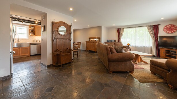 A spacious living area with a sofa, armchairs, and a TV. A kitchen with a sink and cabinets is visible in the background. - Country home just minutes from town (Port Angeles)