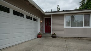 A single-story house with a white garage door, a red front door, and a small front porch with two potted plants. - Country home just minutes from town (Port Angeles)