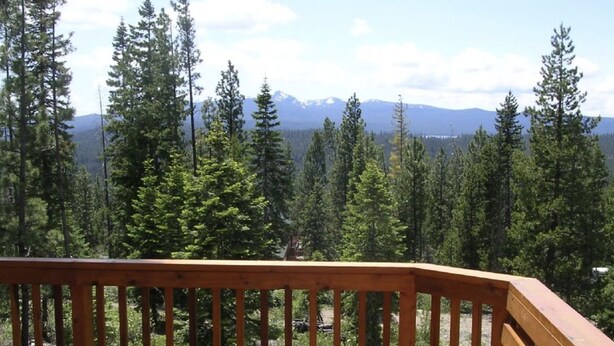 A wooden deck with a bench overlooking a forest and mountains.