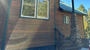 A two-story wooden cabin with large windows, a stone chimney, and a covered porch.