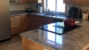 A kitchen with wooden cabinets, a granite countertop, a stainless steel refrigerator, a microwave, a sink, and a red pot on the island.