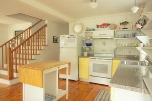 A kitchen with wooden flooring, a wooden staircase, a white refrigerator, a stove, and a sink. - Your Kennebunkport Getaway — Walk to Town! (Kennebunkport)