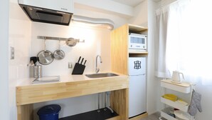 Cocina compacta con estufa integrada, pileta y microondas. Hay una mesada de madera, un bote de basura azul y un carrito pequeño con utensilios de cocina.