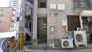 Un edificio con una bicicleta estacionada afuera, unidades de aire acondicionado exteriores y un basurero.