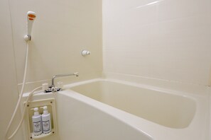 A bathtub with a showerhead, a faucet, and two bottles of shampoo and conditioner. - Wisdom Minoshima Inn (Fukuoka)