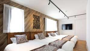 Habitación de hotel con dos camas, cabeceros de madera, un televisor grande montado en la pared y piso de madera.
