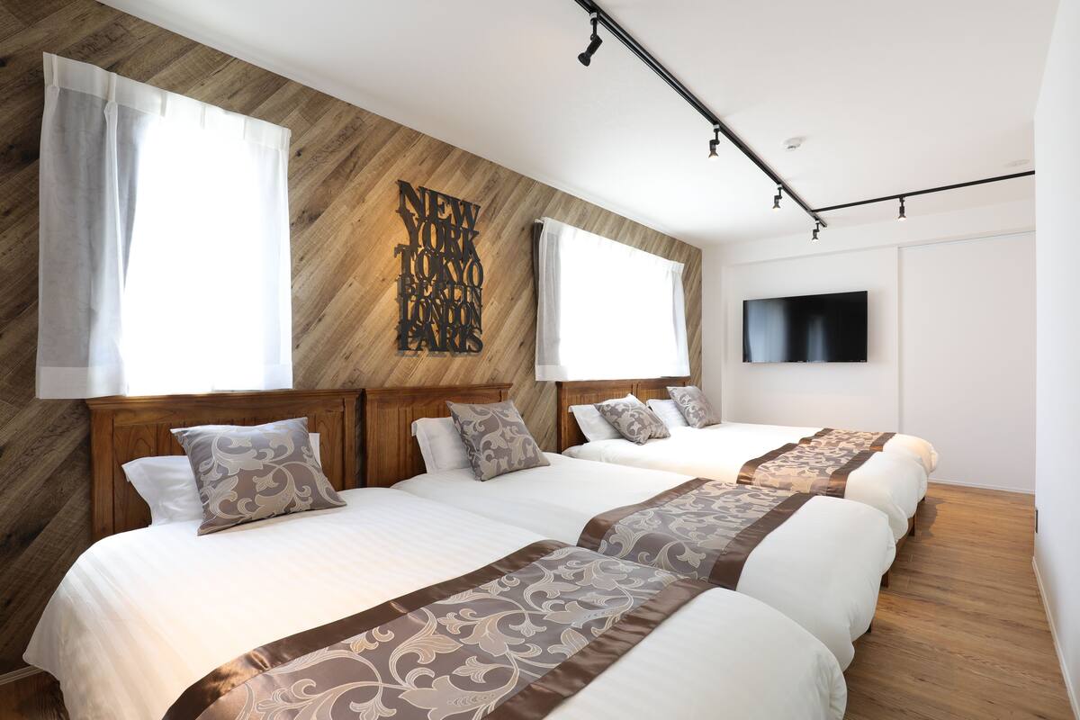 A hotel room with two beds, wooden headboards, a large wall-mounted TV, and a wooden floor.