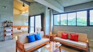 Habitación de hotel moderna con un ventanal grande, un sofá, una mesa de centro de madera y una cama con cabecero.
