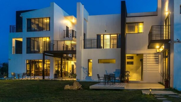 Una casa moderna de dos pisos con amplios ventanales, un balcón y una zona de estar exterior bien iluminada.
