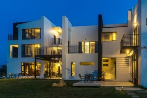 A modern two-story house with large windows, a balcony, and a well-lit outdoor seating area. - Lin's Forest (Hengchun)