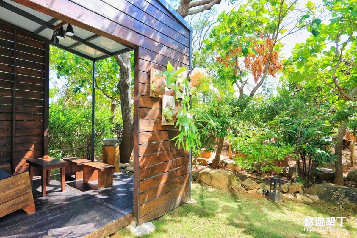 A wooden deck with benches and a table, surrounded by lush greenery and trees.