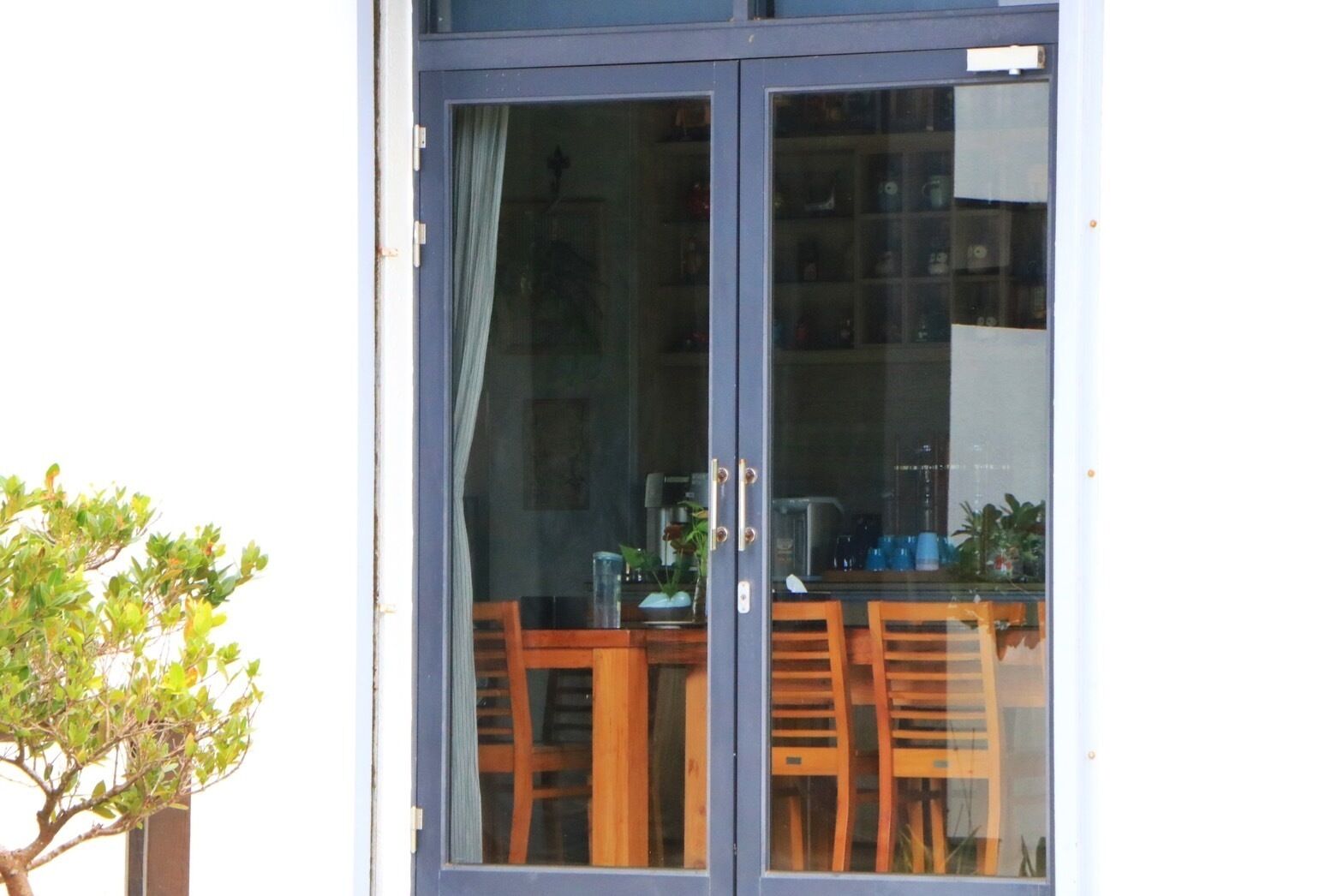 Uma porta de vidro com vista para uma área de refeições, incluindo uma mesa, cadeiras e um vaso de planta lá fora.