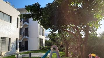 Un bâtiment moderne à l’extérieur blanc, doté d’un balcon et d’une aire de jeux avec un toboggan et des balançoires.