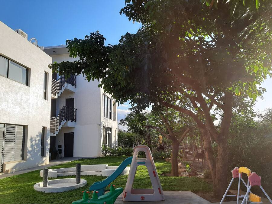 Un bâtiment moderne à l’extérieur blanc, doté d’un balcon et d’une aire de jeux avec un toboggan et des balançoires.