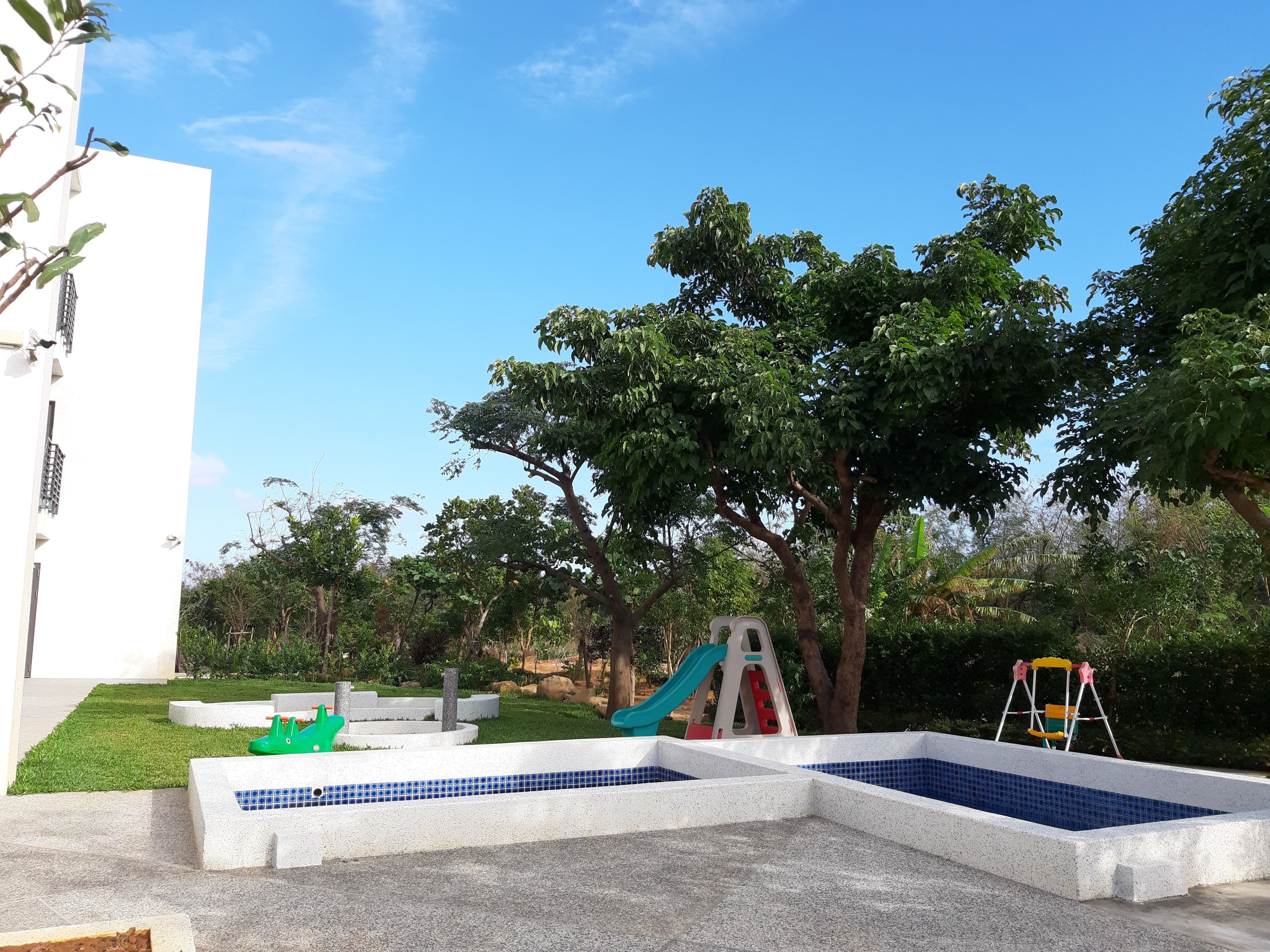 Uma área de recreação infantil com uma piscina pequena, um escorrega e baloiços.