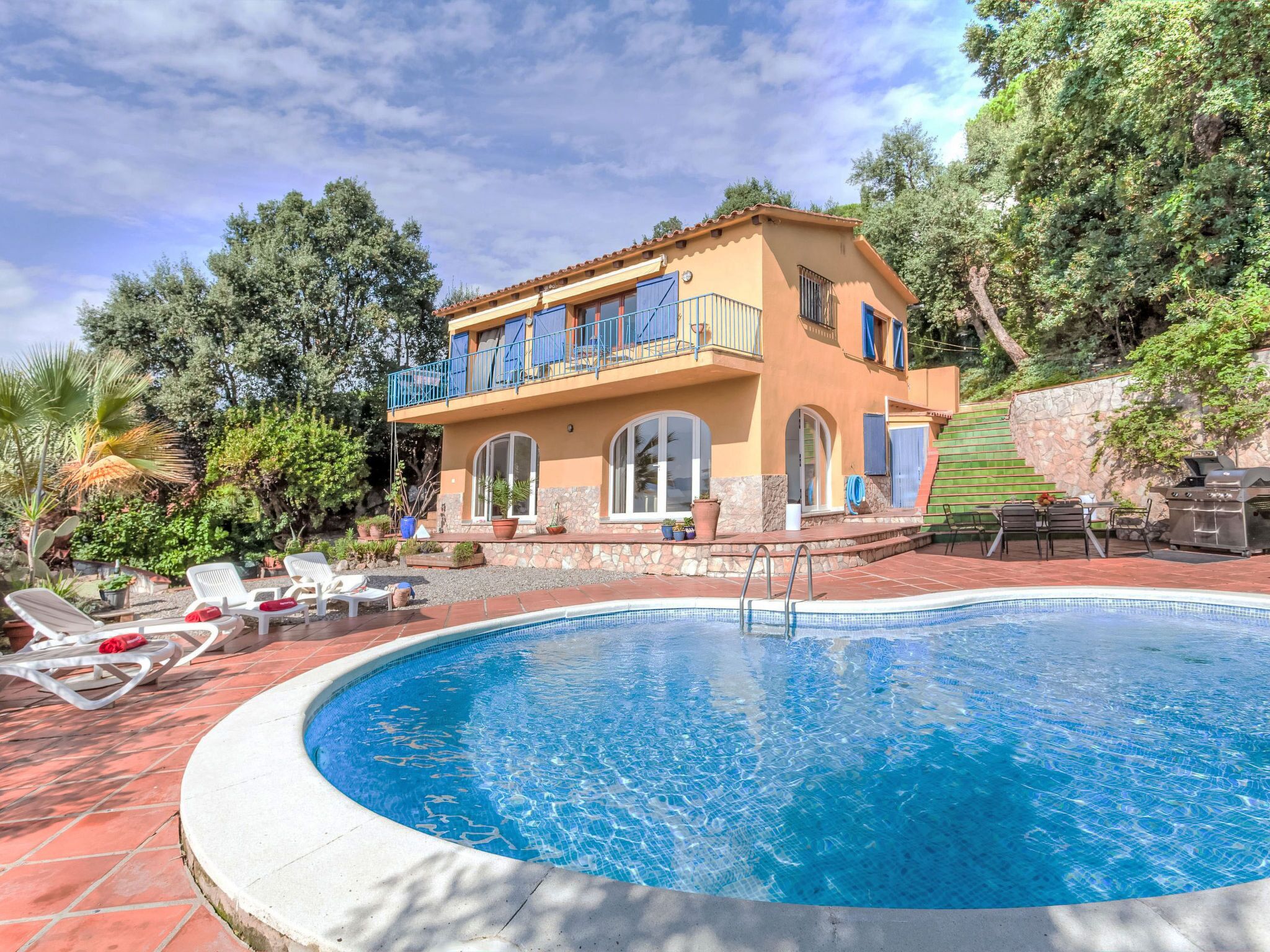 Une maison à deux étages avec une piscine, du mobilier d’extérieur et un mur en pierre.