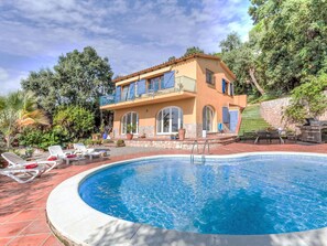 Una casa de dos pisos con piscina, muebles de exterior y un muro de piedra.