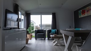 Een moderne woonkamer met een televisie, een eettafel, twee stoelen, een plant en een groot raam.