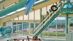 Een overdekt waterpark met een lange glijbaan, een zwembadgedeelte en een uitkijkpunt met grote ramen.