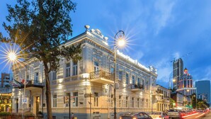 Un edificio histórico con arquitectura clásica, una calle empedrada y modernos rascacielos al fondo.