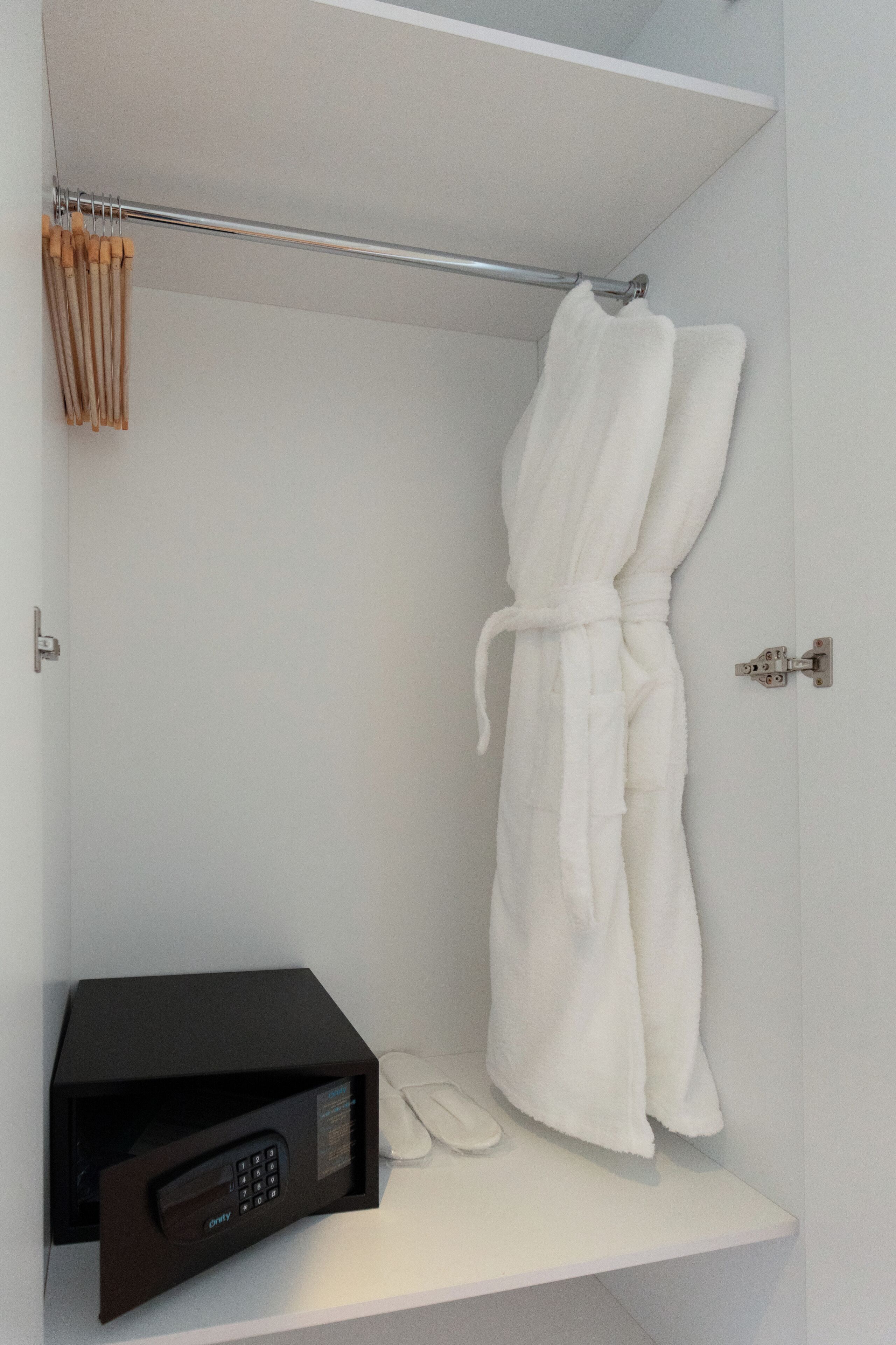 A bathroom with a white bathtub, a white robe hanging on a towel rack, and a black microwave on a shelf.