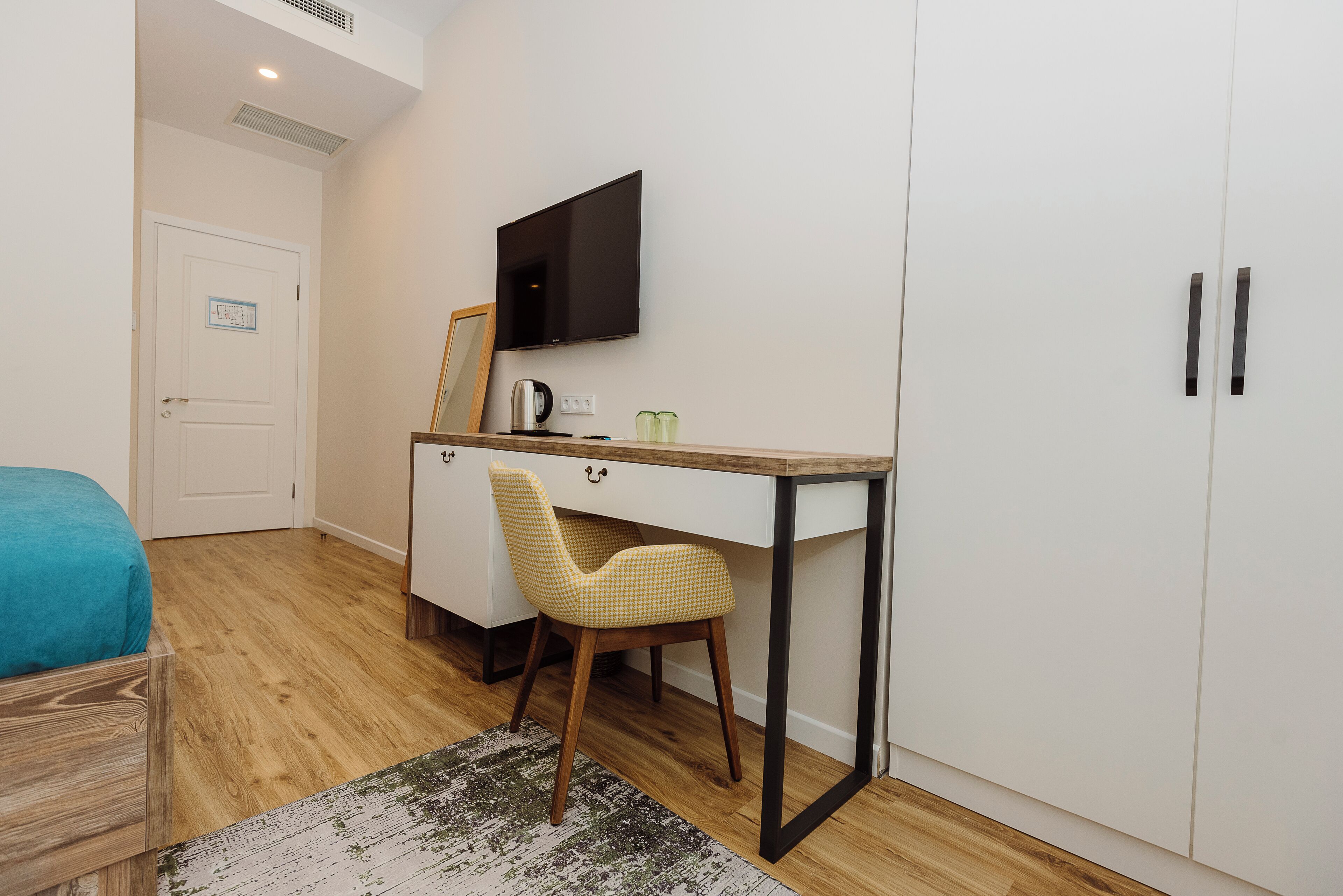 A bedroom with a bed, a desk, a chair, a television, and a wardrobe.