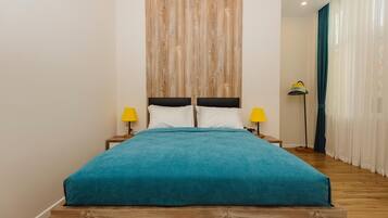 A bed with a teal bedspread, wooden headboard, and two bedside tables with yellow lamps.