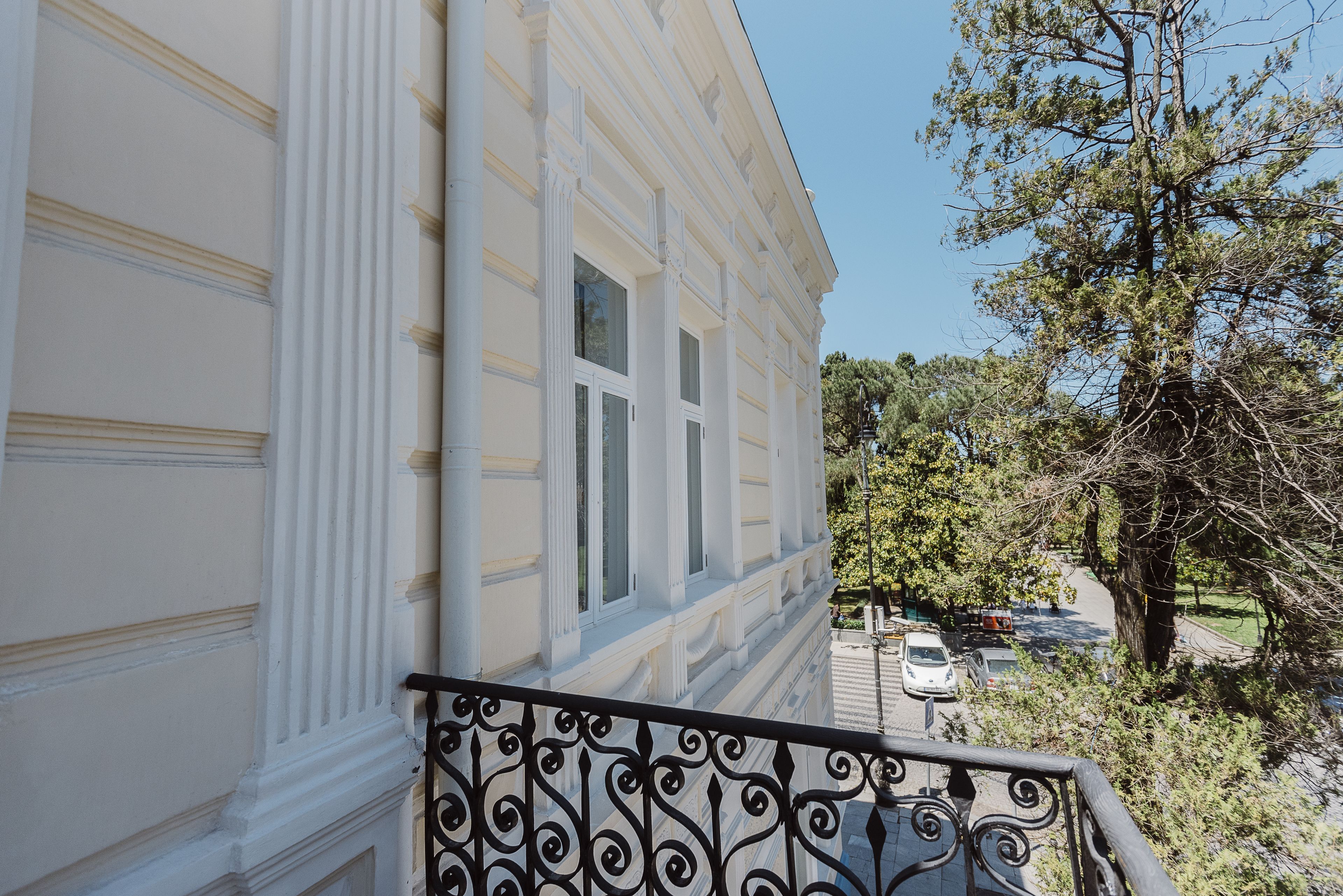 Ένα λευκό κτίριο με μεγάλα παράθυρα και ένα μπαλκόνι με περίτεχνο μαύρο κάγκελο.
