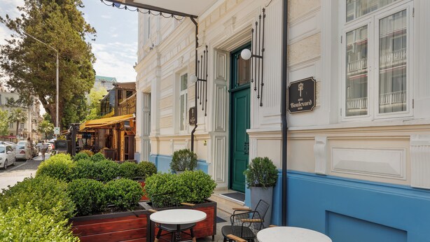 Exterior de un hotel con mesas al aire libre, una puerta verde y un letrero que dice "Boulevard Hotel".
