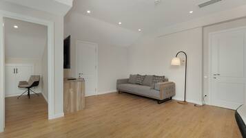 A modern living room with a grey sofa, wooden flooring, white walls, and recessed ceiling lights.