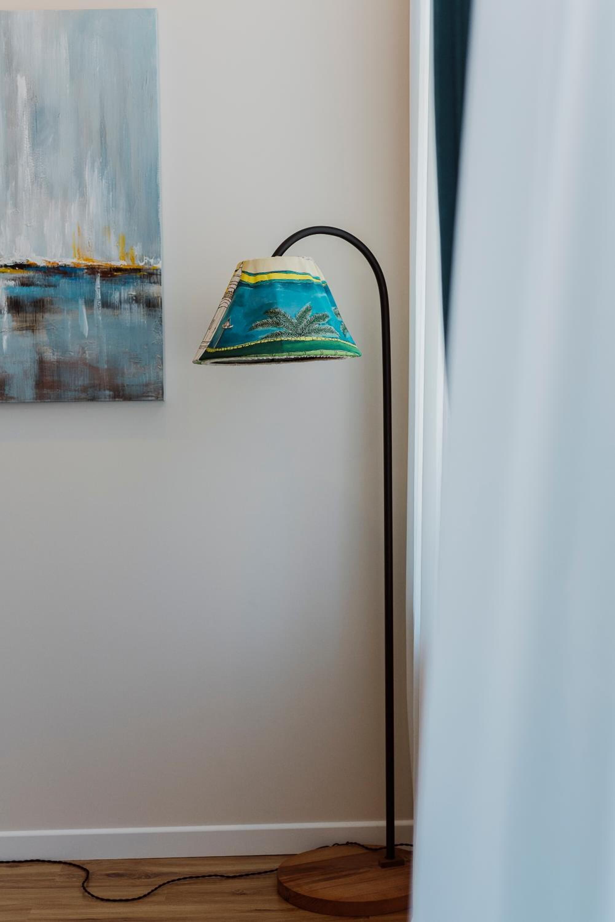 Ein Zimmer mit Stehlampe, einem Gemälde an der Wand und Holzboden.