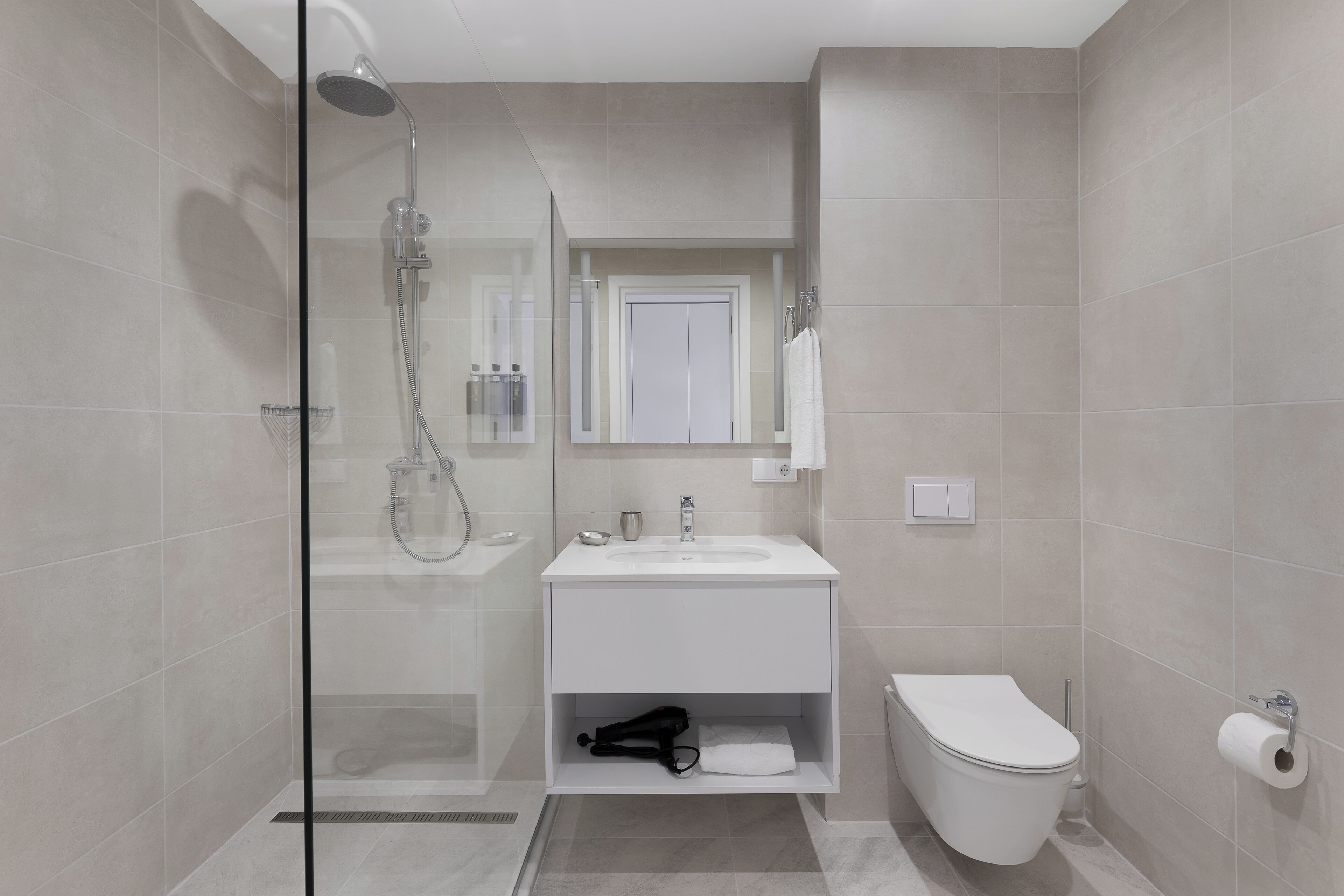 Un baño moderno con ducha de vidrio, lavamanos blanco y inodoro.