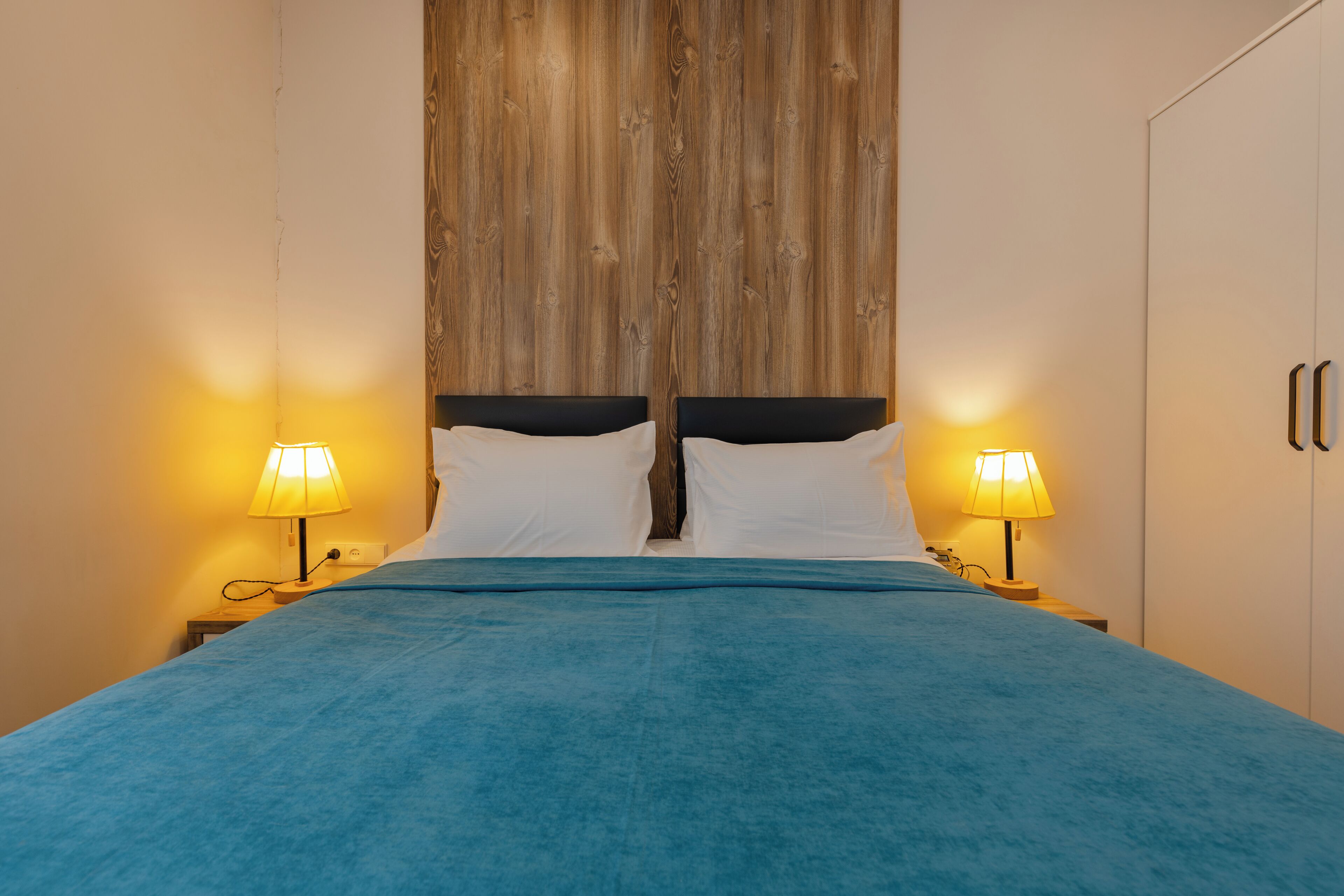 A bed with a blue bedspread, two bedside lamps, and a wooden headboard.