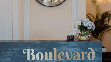 A reception desk with a clock above it and a vase of flowers to the right. The text "Boulevard Hotel Batumi" is visible on the desk.