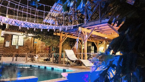Un área de piscina con cubierta de madera, sillas de descanso y un puente colgante.