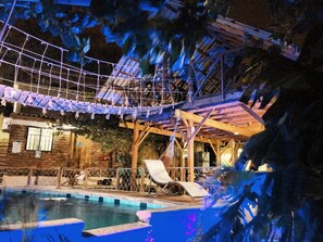 A pool area with a wooden deck, lounge chairs, and a rope bridge. - Hostal Kaia - Hostel (Santa Marta)