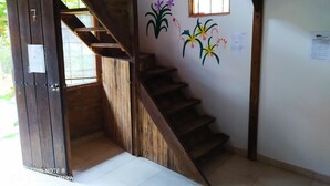Una escalera de madera que lleva a una habitación con pared blanca y una ventana pequeña.