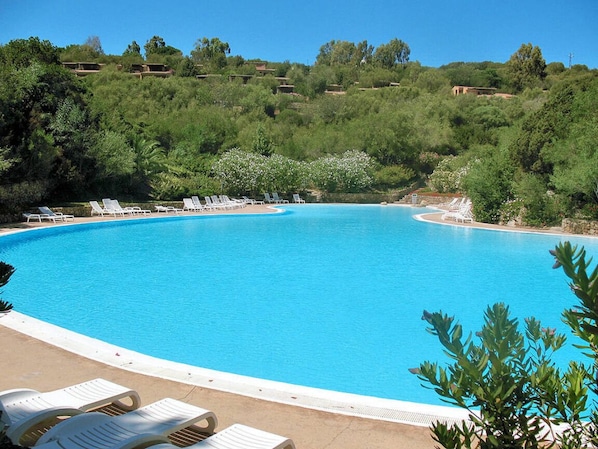 A large, clear blue swimming pool surrounded by white lounge chairs, set against a backdrop of lush greenery and hills. - Villino Federico - A splendid resort immersed in the greenery of Cala Capra (Palau)