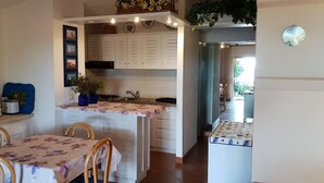 Een kleine keuken met witte kastjes, een magnetron, een fornuis en een eethoek met een tafel en stoelen.